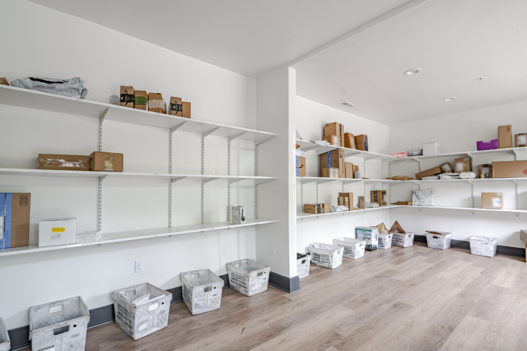 Package room with wood-look flooring, white walls, a white ceiling, wall-mounted shelving, and package storage bins.
