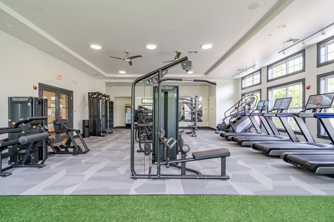 Fitness center with patterned gray flooring, white walls, a white ceiling, cardio machines, strength equipment, and large windows.