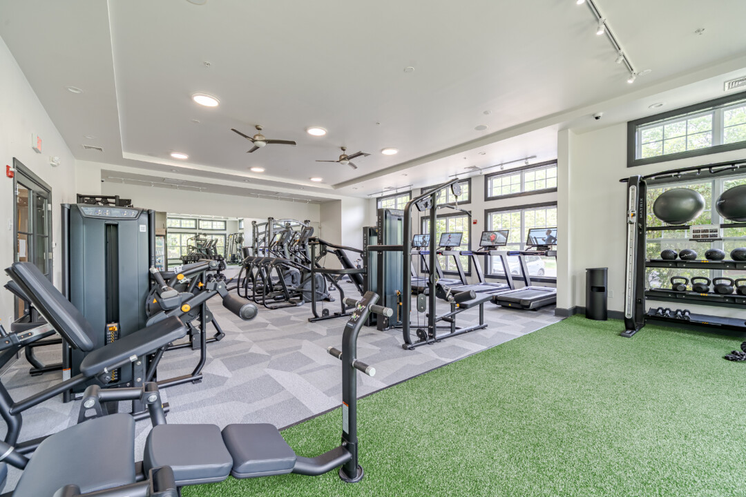 Fitness center with green turf flooring, patterned gray flooring, white walls, a white ceiling, and exercise equipment.