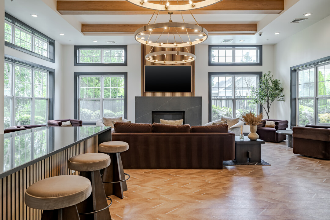 Community lounge with wood-look flooring, white walls, a white ceiling with wood beams, large windows, a fireplace, and upholstered seating.