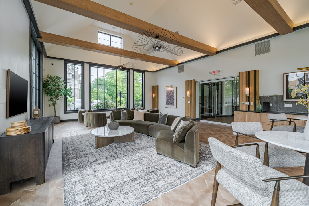 Community lounge with wood-look flooring, white walls, a vaulted white ceiling with wood beams, upholstered seating, and large windows.