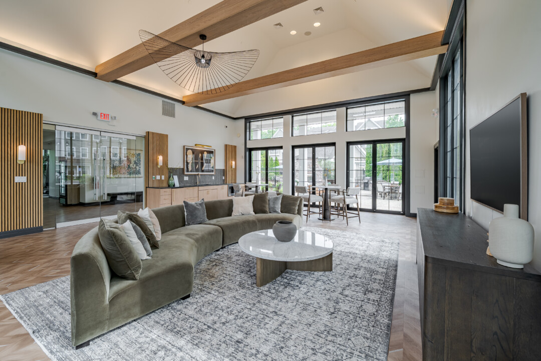 Community lounge with wood-look flooring, white walls, a vaulted white ceiling with wood beams, upholstered seating, and glass doors leading to an outdoor patio.