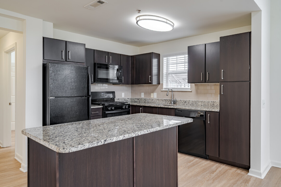 Kitchen with dark wood cabinets, light stone countertops, black appliances, wood-look flooring, light-colored walls, and a white ceiling.