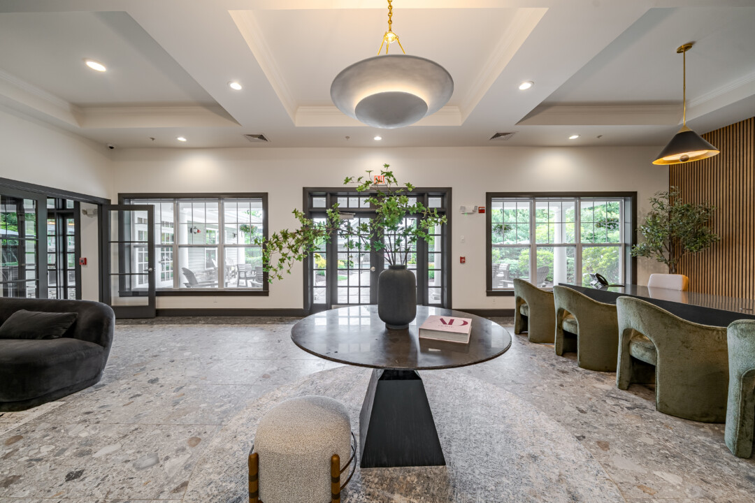 Lobby with stone-look flooring, light-colored walls, a white ceiling with recessed lighting, upholstered seating, and large windows.