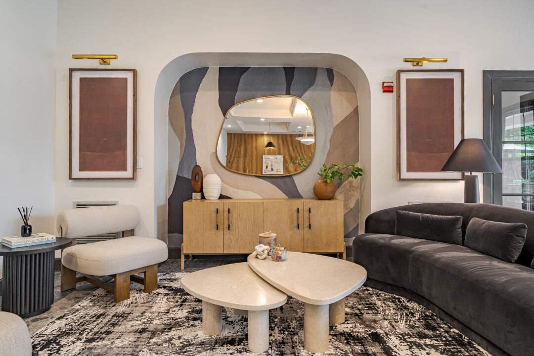 Lobby lounge with stone-look flooring, light-colored walls, a white ceiling, upholstered seating, a wood cabinet, and decorative wall art.