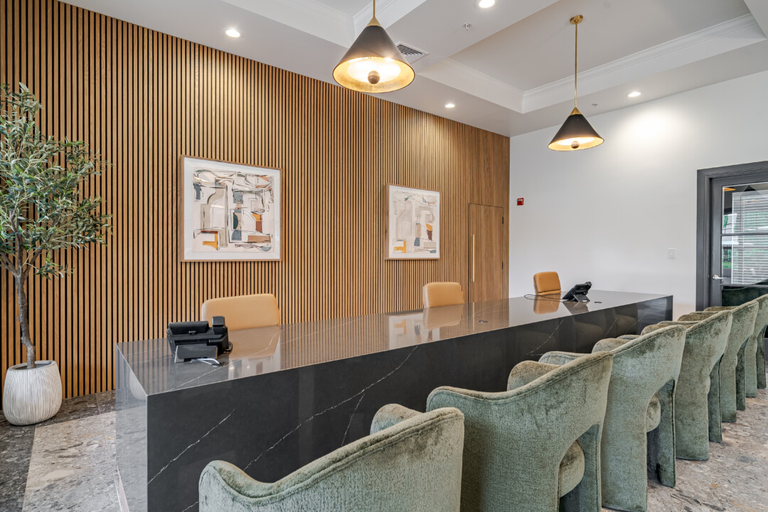 Reception area with stone-look flooring, light-colored walls, a wood slat accent wall, a dark reception desk, and upholstered guest chairs.