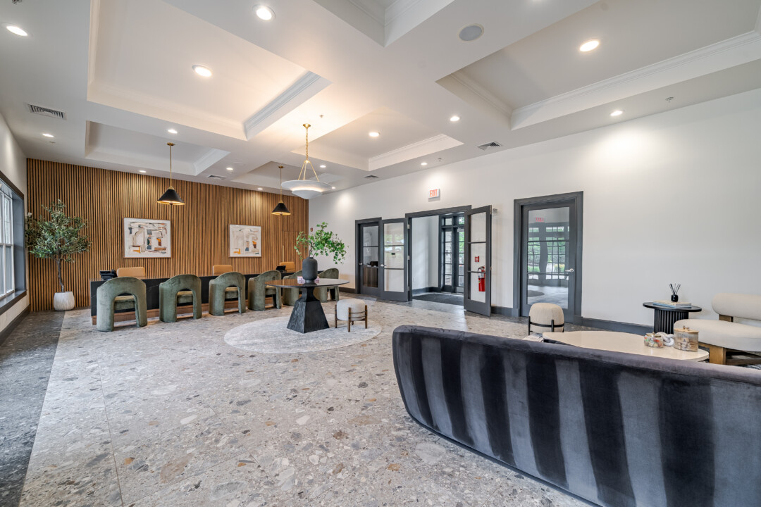 Lobby with stone-look flooring, light-colored walls, a white ceiling with recessed lighting, lounge seating, and a reception desk.