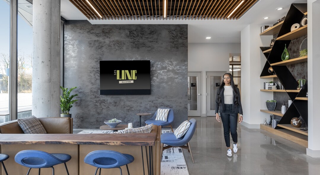 Community lounge with seating, a wall-mounted TV on a gray accent wall, and large windows.