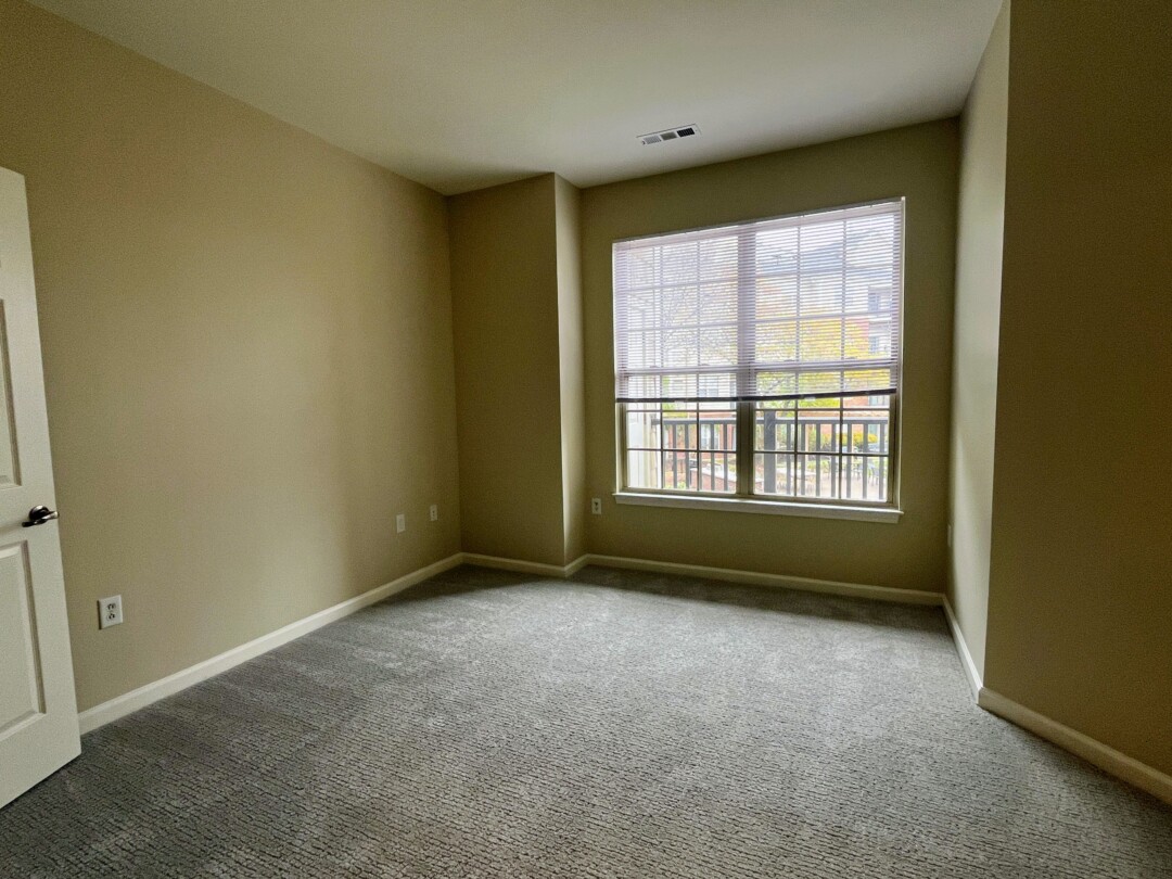 Spacious bedroom with carpet, soft neutral walls, and a white ceiling with air vent; window with white blinds.