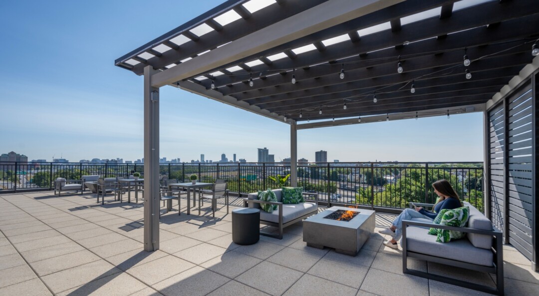 Rooftop deck with large tile flooring, covered seating area, fire pit, and city skyline views.