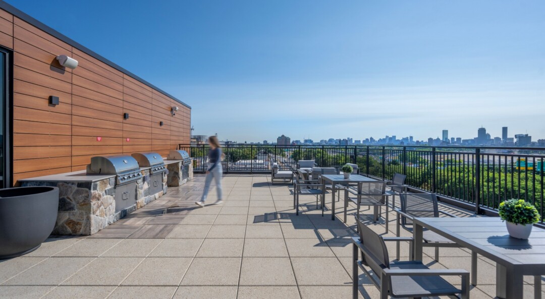 Rooftop deck with large tile flooring, outdoor seating, grilling stations, and city skyline views.