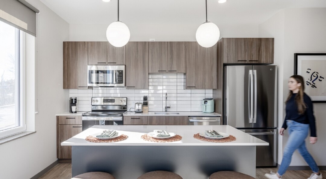 Kitchen with white walls, wood cabinets, white tile backsplash, and a kitchen island with countertop seating.