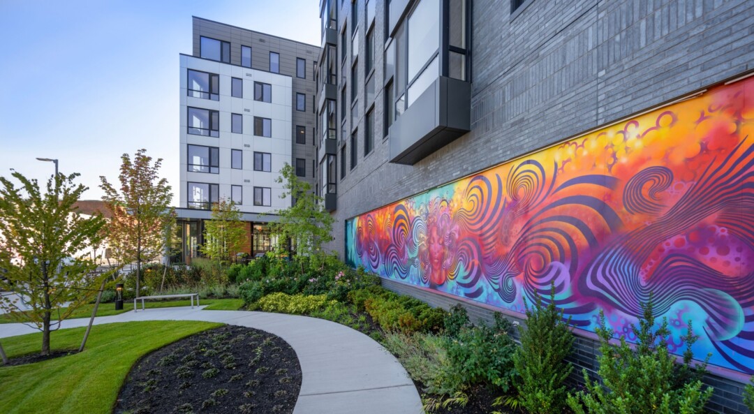 Colorful mural on an exterior wall along a landscaped walkway.