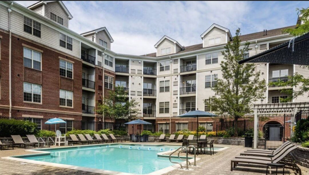 Thes Avens at Newton Highland outdoor pool with patio area of tables and chairs behind apartment building