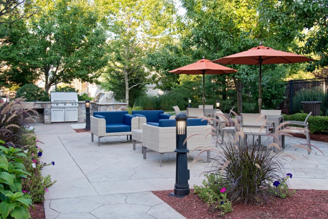 Outdoor patio with barbecue grills, blue lounge seating, dining tables, and umbrellas.