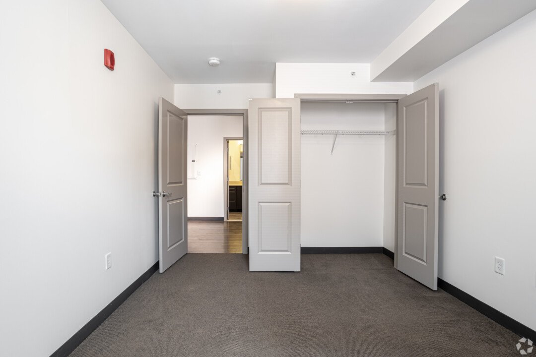 Bedroom with dark carpet flooring, white walls, a white ceiling, and an open closet with double doors.