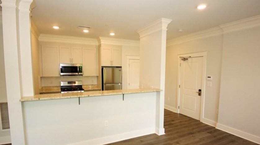 Kitchen with white cabinets, light stone countertops, stainless steel appliances, wood-look flooring, light gray walls, and a white ceiling with recessed lighting.
