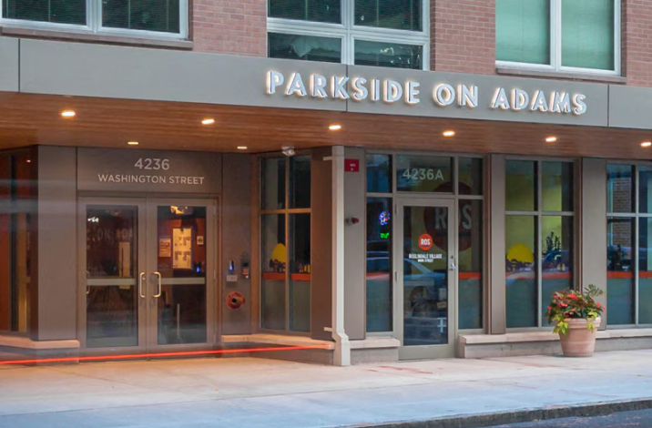 Main entrance of the apartment building with large glass doors, exterior lighting, and building signage.