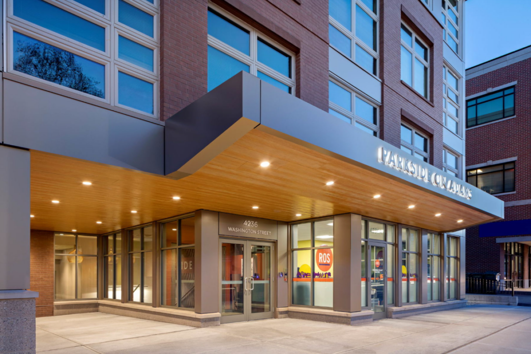 Apartment building entrance with glass storefront windows, exterior lighting, and illuminated entryway at night.