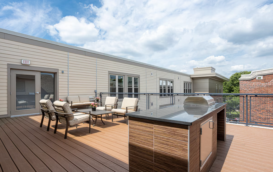 Rooftop deck with wood decking, outdoor seating, a grill island, and open sky views.