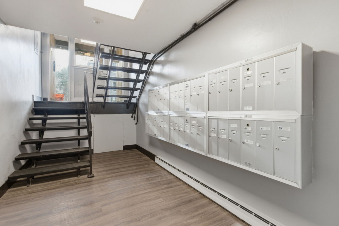 Building mail area with rows of white mailboxes, light wood flooring, and a staircase.