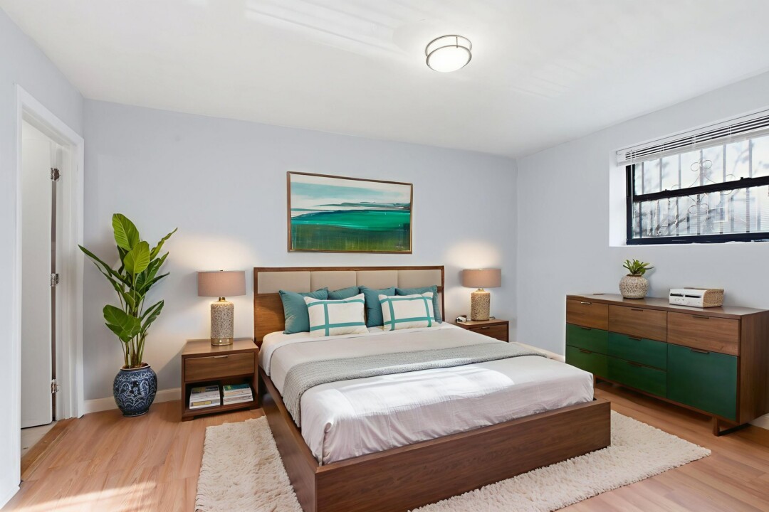 Furnished bedroom with a bed, two bedside tables with lamps, wood flooring, wall art, and a dresser.