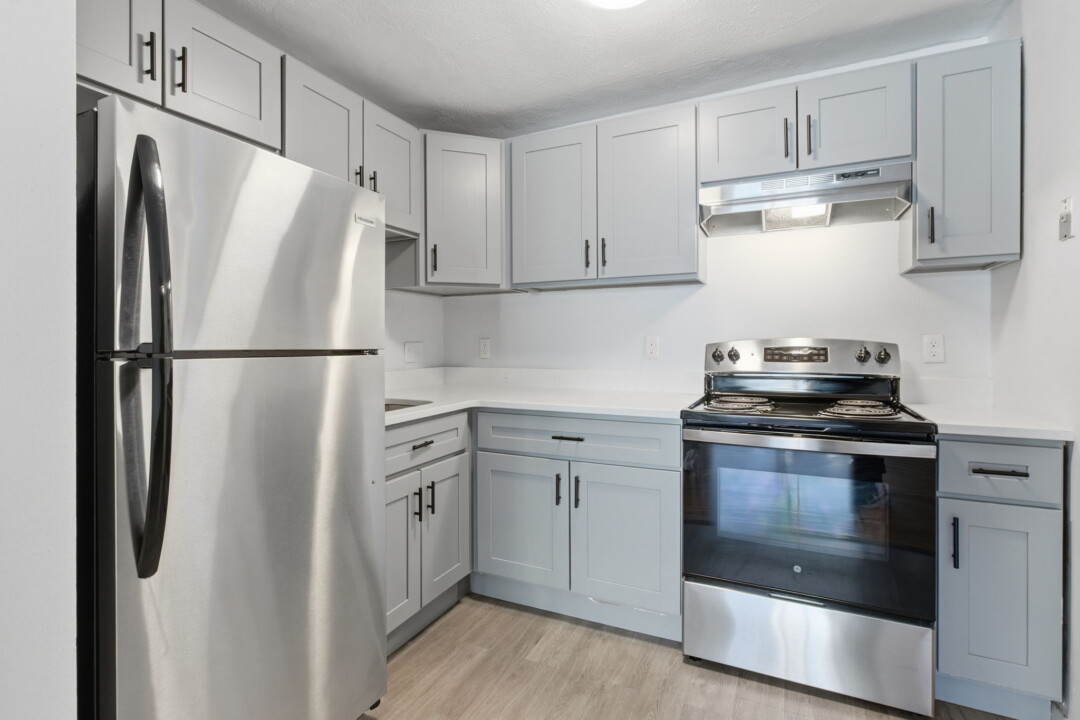 Kitchen with light gray cabinets, stainless steel appliances, white countertops, and light wood flooring.