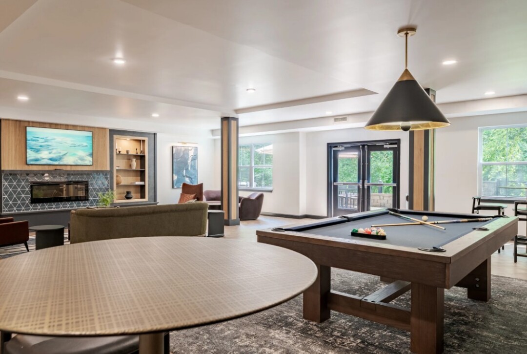 Community game room with a pool table, seating area, large windows, and pendant lighting.