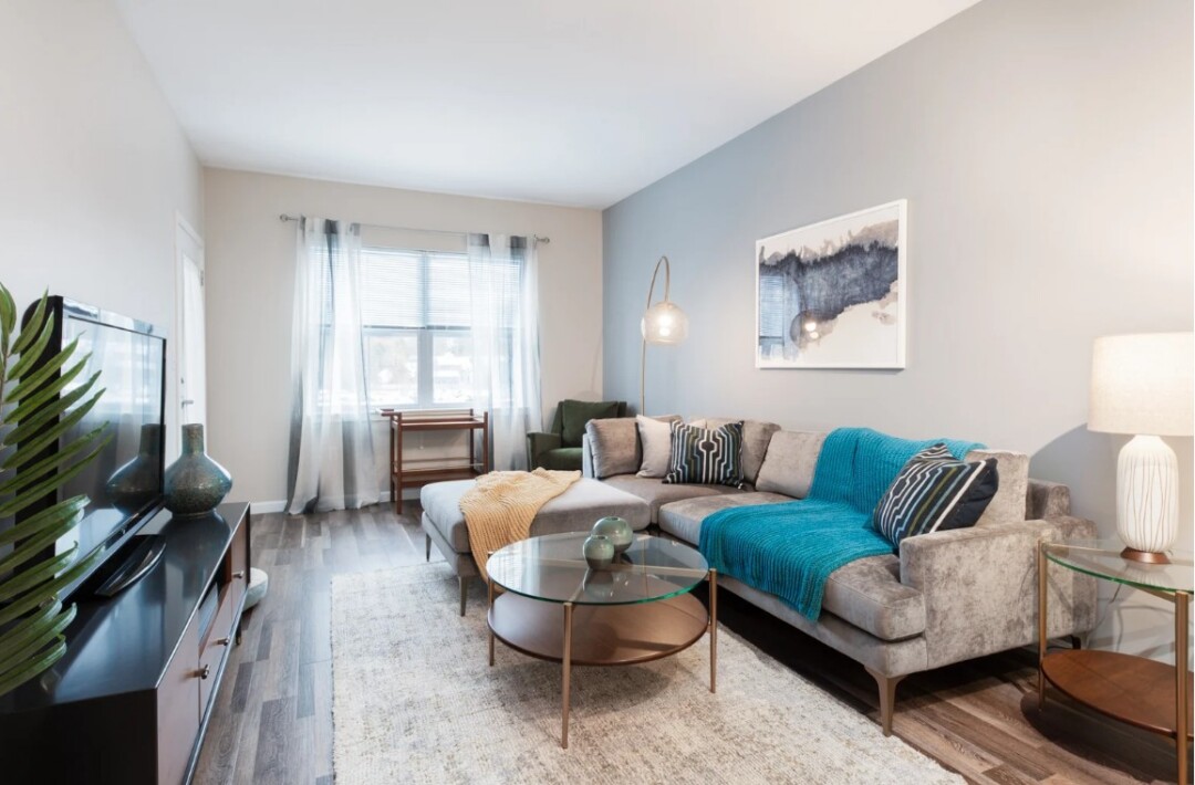 Furnished living room with a sofa, coffee table, large window, and wood flooring.