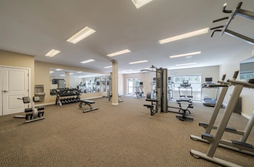 Spacious fitness center with exercise equipment, large mirrors, carpeted flooring, and overhead lighting.