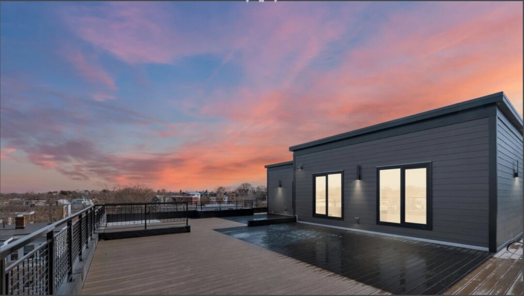 Spacious rooftop deck with dark railings and wood flooring under a colorful pink and orange sunset sky.