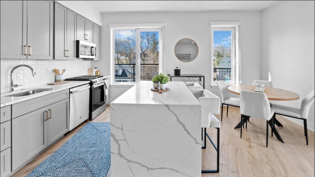 Modern kitchen with gray cabinets, stainless steel appliances, a large white island, light wood flooring, and a dining table with chairs.