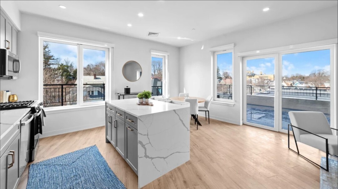 Bright kitchen with gray cabinets, a large white island, light wood flooring, and large windows and glass doors.