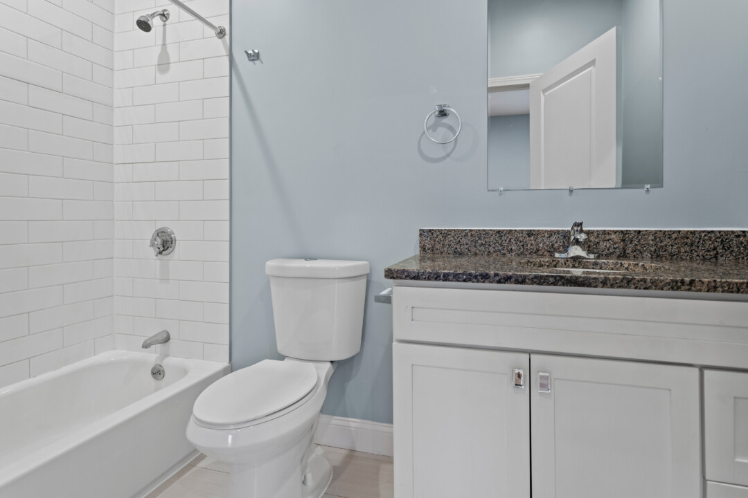 Bathroom with a tiled bathtub and shower, toilet, and white vanity with a dark countertop.