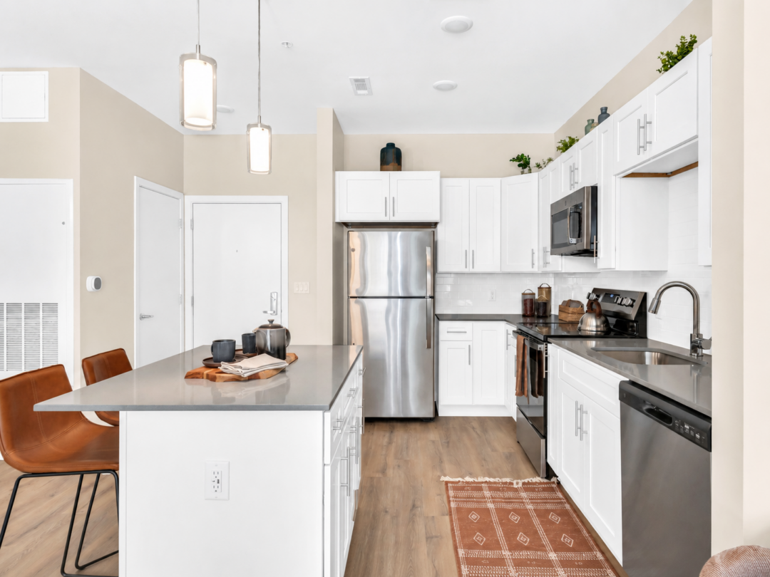Apartment kitchen with white cabinets, an island, wood-look flooring, and stainless steel appliances.