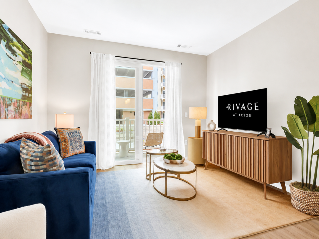 Living room with a blue sofa, round coffee table, television, and glass doors opening toward a balcony.
