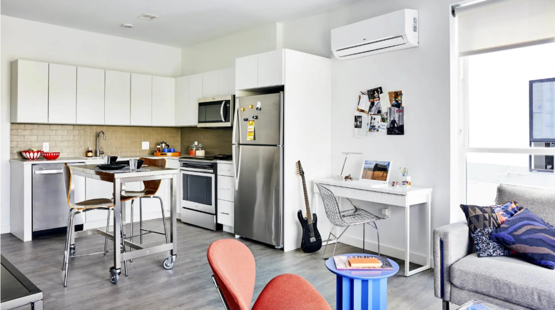 Open kitchen and living area with white cabinets, stainless steel appliances, a desk, and a sofa.