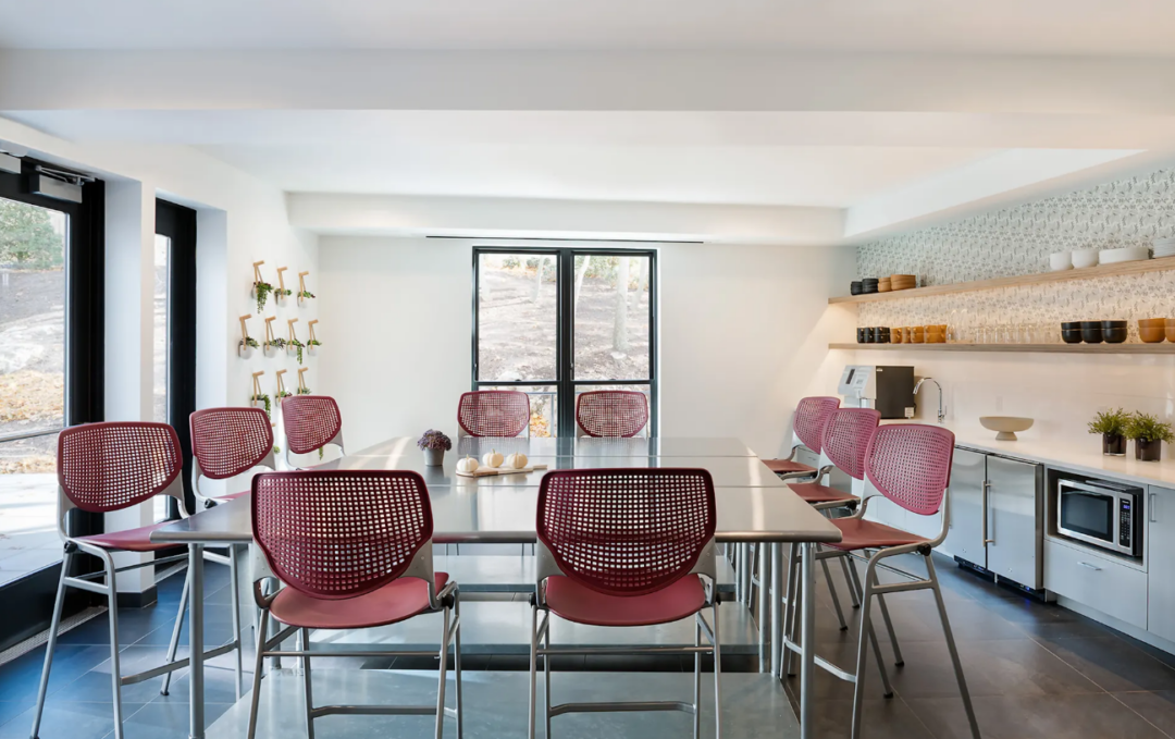 Shared dining area with tall tables, red stools, and a kitchenette.