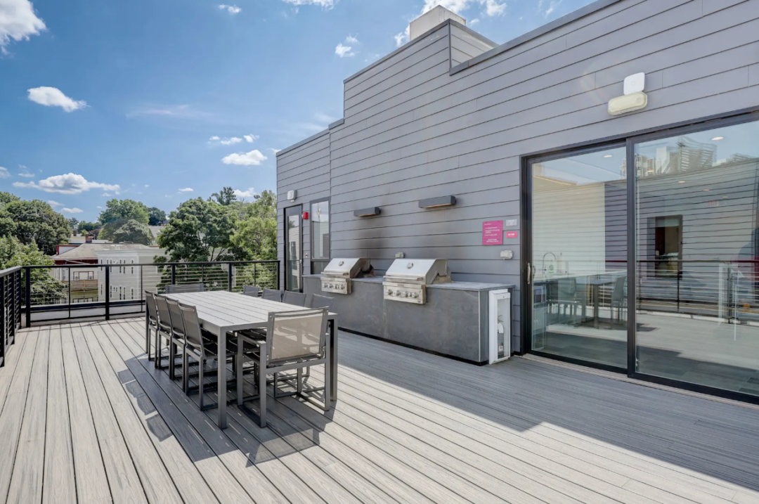 Rooftop deck with a dining table, chairs, and two built-in grills beside sliding glass doors.