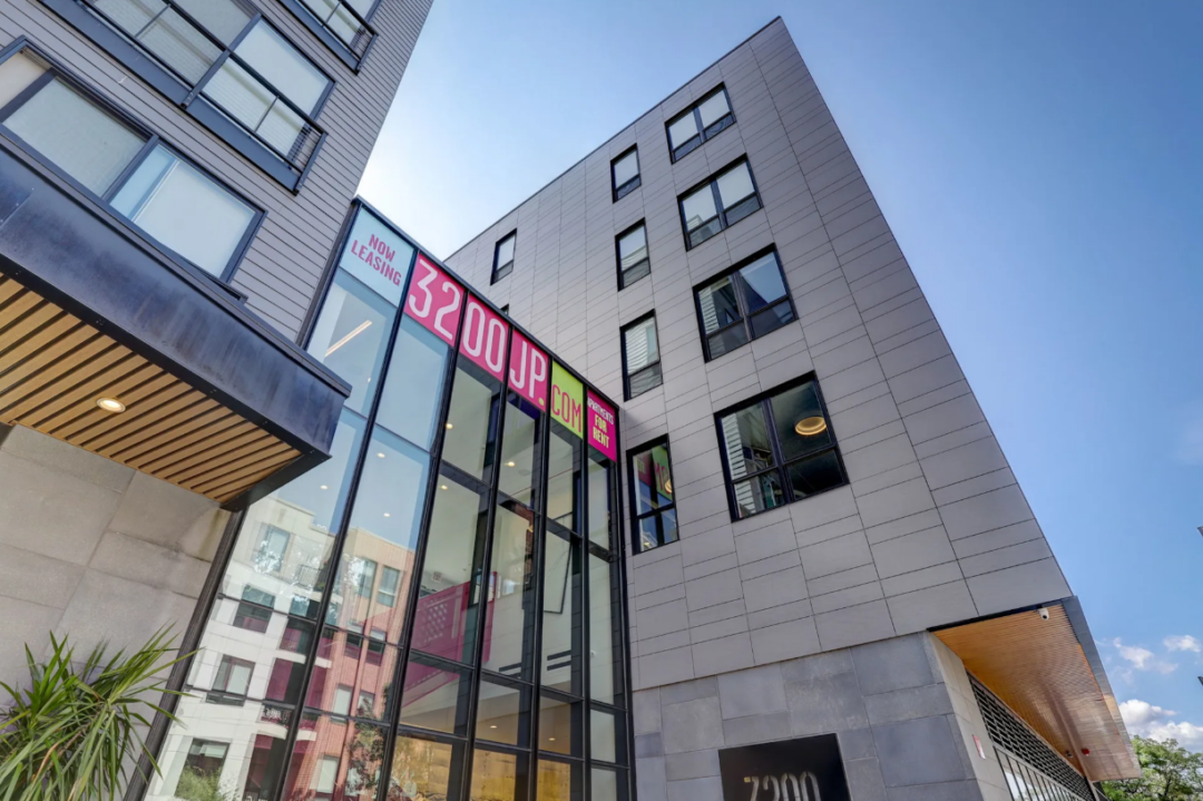 Apartment building exterior with tall glass windows and a leasing sign.