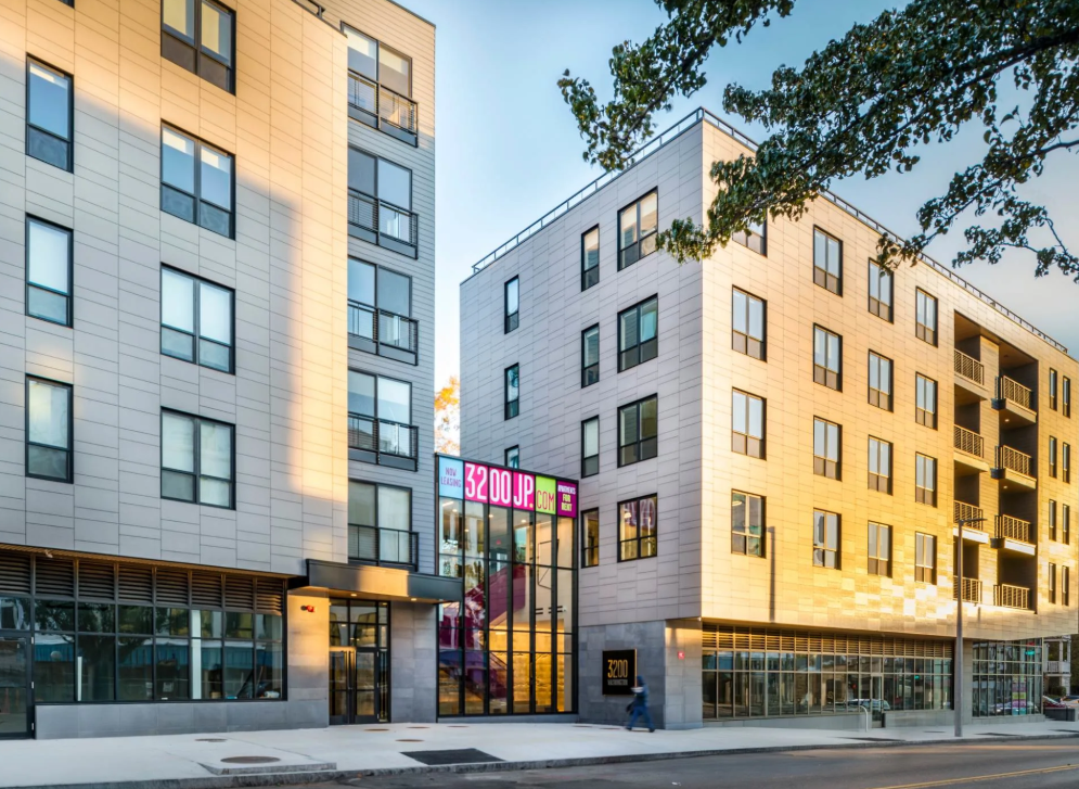 Apartment building exterior with large windows, balconies, and a glass entrance.