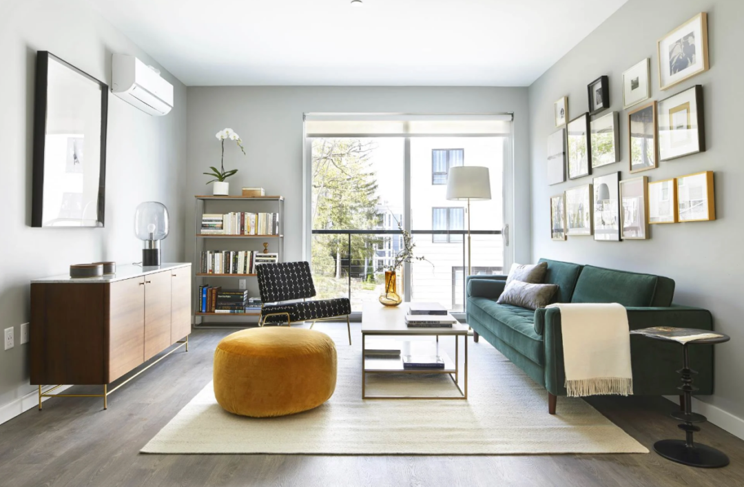 Living room with a teal sofa, patterned chair, yellow ottoman, and framed wall art.