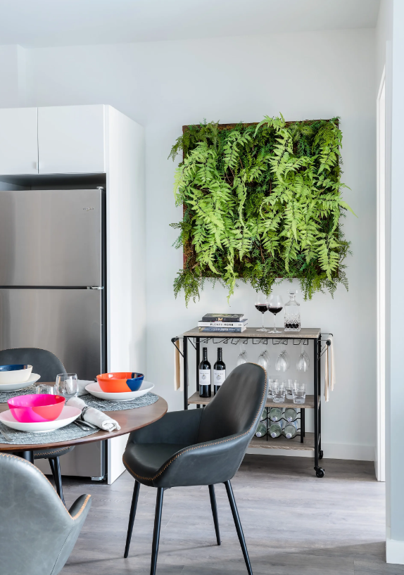 Dining area with a round table, chairs, and a bar cart beneath a wall-mounted plant display.