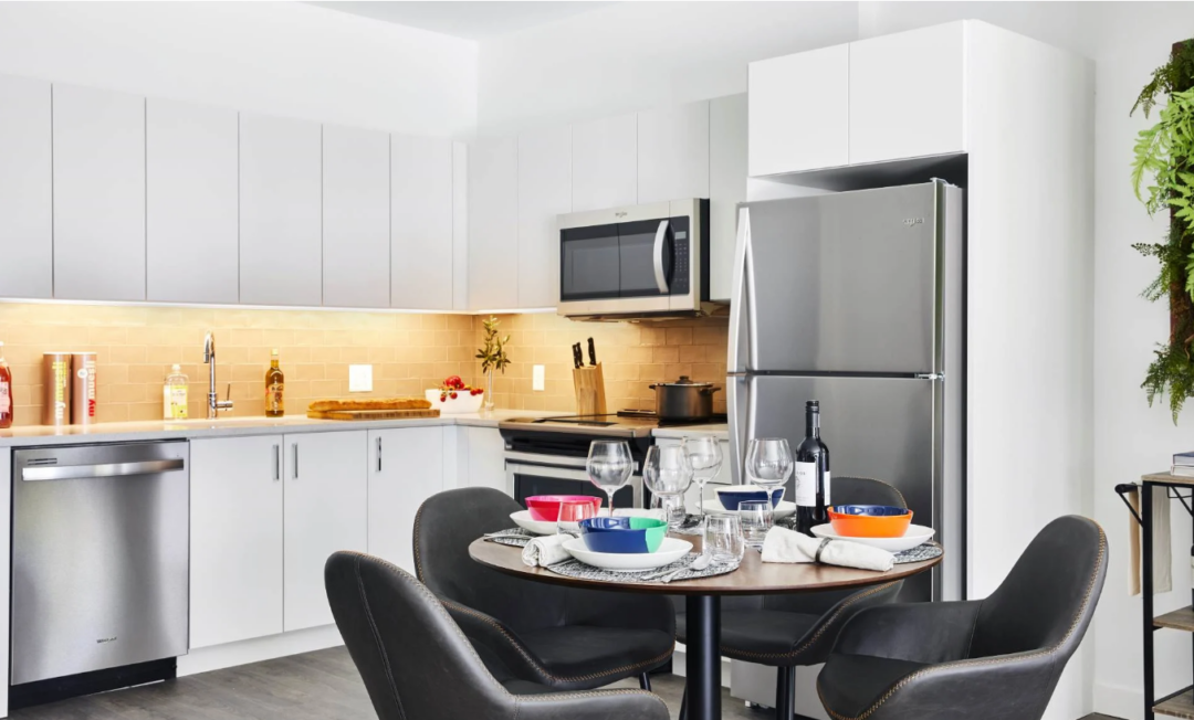 Kitchen with white cabinets and stainless steel appliances beside a dining table set for four.