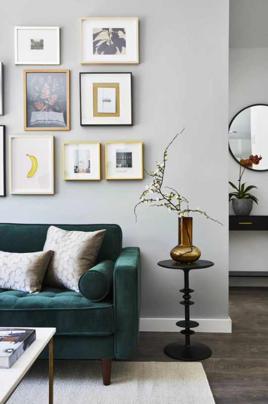 Teal sofa beneath framed wall art beside a black side table with a vase.