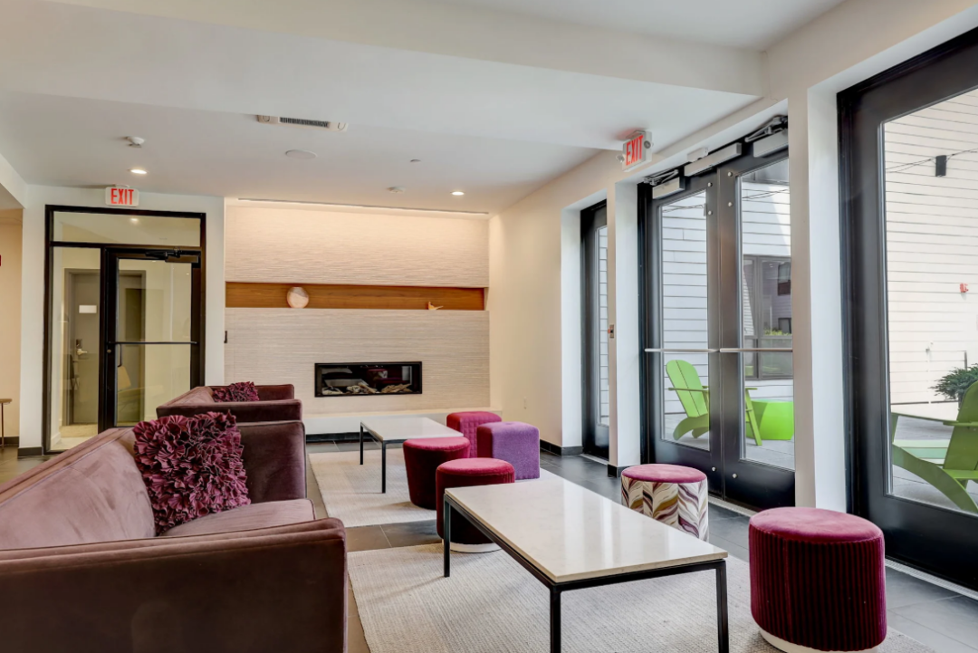Lounge with sofas, stools, coffee tables, and a fireplace beside glass patio doors.