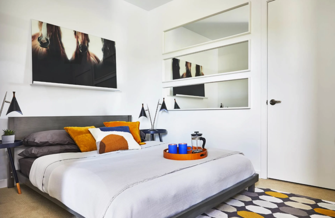 Bedroom with a bed, colorful pillows, bedside lamps, and horizontal wall mirrors.