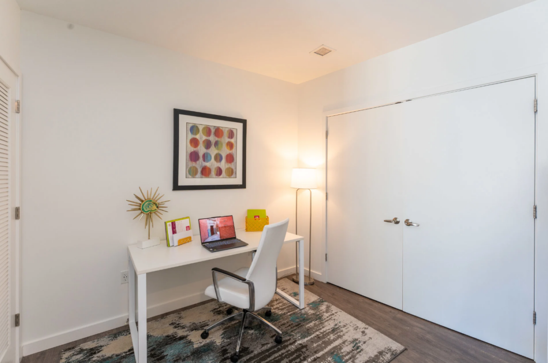 Home office with a white desk, laptop, rolling chair, and double closet doors.