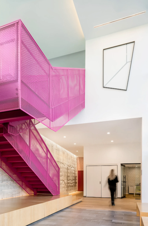 Lobby with a bright pink metal staircase and built-in wooden bench.