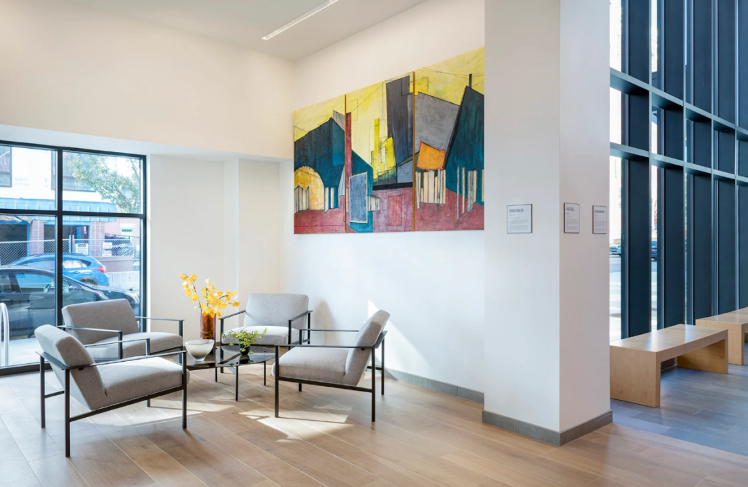 Lobby seating area with four armchairs, a glass coffee table, and colorful wall art.